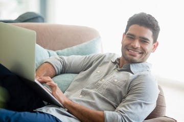 Fototapeta premium Man sitting on sofa and using laptop in living room at home