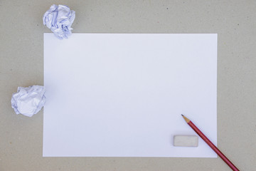 An A4 paper laid on a grungy brown paper background with two crumpled paper balls, red wooden pencil and a white rubber on its sides