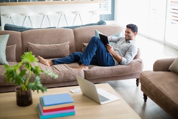 Obraz premium Man sitting on sofa and using digital tablet in living room