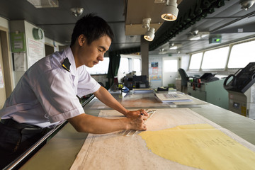 Young Chinese Navigator Doing Chartwork on Bridge