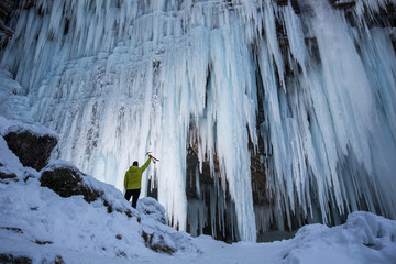Ice climber is checking frozen waterfall for the next extreme outdoor adventure. Reaching, planning, out of comfort zone, dedication concept photo.