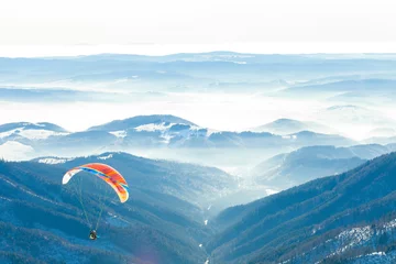 Rolgordijnen Paragliders gelanceerd in de lucht vanaf de top van een besneeuwde helling van een berg © niyazz