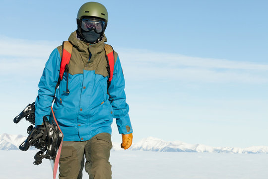 Snowboarder holding snowboard in hand and walking at the top of a mountain