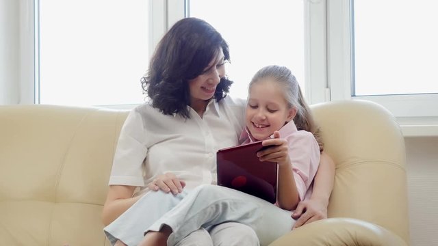Mother with daughter using tablet computer, laughing and looking in digital tablet.