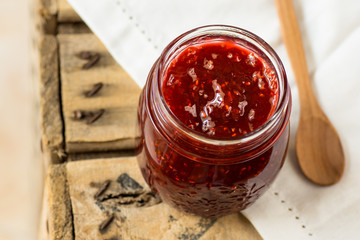 Jar with homemade raspberry jam with wooden spoon, on white linen napkin, top angle view,cozy morning atmosphere,breakfast
