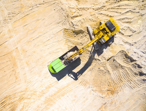 Aerial view of a excavator loading a truck in the mine or on construction site. Heavy industry from above. Industrial background with drone photography.