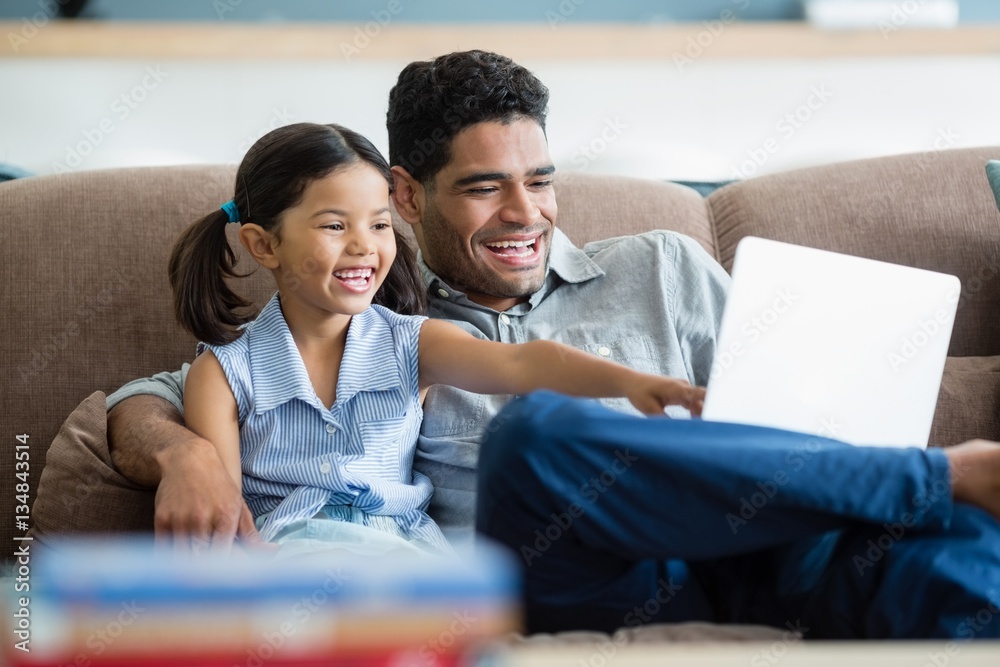 Canvas Prints Father and daughter sitting on sofa and using laptop