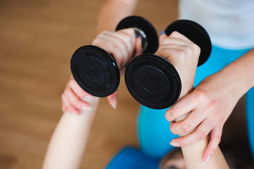 Personal coach helping woman to do exercises with dumbbells in g