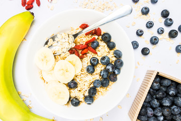 Top View Oat Flakes with Banana Slices, Blueberries and Wolfberries on White Background