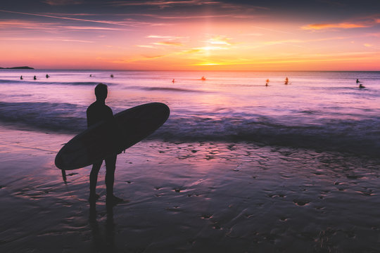 Silhouette Of Surfer Man Holding Surfboard On Beach At Sunset