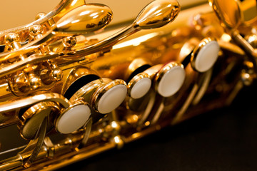 Obraz na płótnie Canvas Fragment of a saxophone valves in gold tones on a dark background