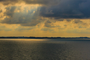 Beautiful sunrise over the sea in the morning on cloudy day that sun beams break through the clouds. Sun beaming through clouds with urban landscape, if you zoom in will see the small fishing boats.