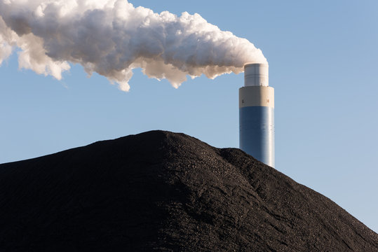Pile of coal with the chimney of a coal power plant behind