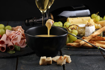 Gourmet Swiss fondue dinner on a winter evening with assorted cheeses on a board alongside a heated...