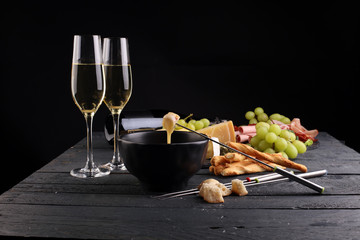 Gourmet Swiss fondue dinner on a winter evening with assorted cheeses on a board alongside a heated...