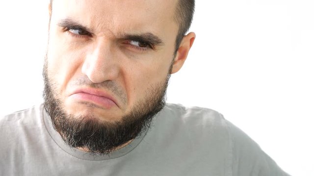 Close-up of angry young bearded man face frowning, studio isolated on white background.