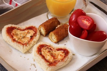 Heart shaped Bread pizza served in a tray with orange juice Mozzarella sticks and cherry tomatoes