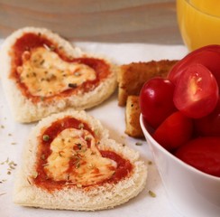 Heart shaped Bread pizza served in a tray with orange juice Mozzarella sticks and cherry tomatoes
