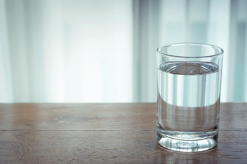 Glass of water on wooden table and light blurred background.