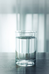 Glass of water on wooden table and light blurred background.