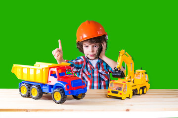 Fototapeta na wymiar Little curly foreman indicates the index finger, talking on the phone next to the toy construction equipment. Close-up. Green background.