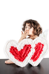 Cute angel sitting on a black floor half-turned and sent a kiss to the camera. Close-up. White background.