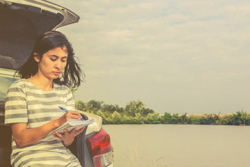 young woman sitting on hatchback and drawing in notebook
