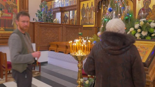 a Man and a Woman Pray Before an Iconostasis, Which Looks Majestic With Its Golden Looking Icons, Images of Saints, Decorated Fir Trees and so on