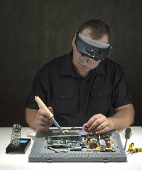 a men at table with a soldering iron, solder computer monitor. 