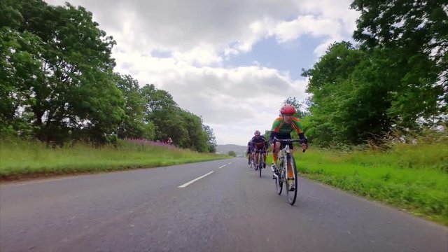 A stabilised view of a group of cycling athletes out on a training ride on country roads in the UK countryside on a sunny day. 