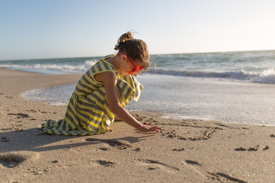Young girl drawing in sand by shoreline