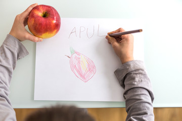 Hands of child drawing and writing apple 