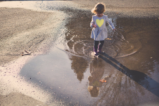 Girl looking at self image in puddle on sand 