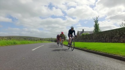 A stabilised view of a group of cycling athletes out on a training ride on country roads in the UK countryside on a sunny day. 