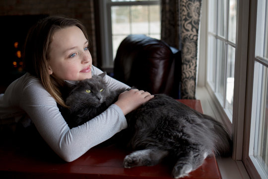 Girl and cat cuddling, looking through window 