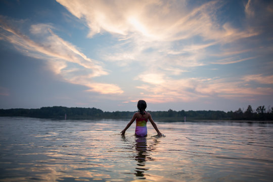 Rear view of girl walking in lake at sunset