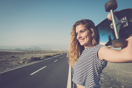 Spain, Tenerife, portrait of smiling young woman with longboard standing at empty country road