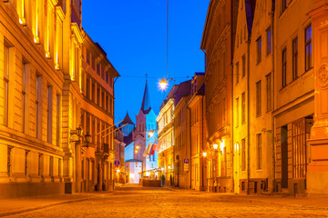 Fototapeta na wymiar Illuminated street in old part of Riga by night. The Our Lady of Sorrows Church.