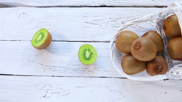 Humans hands chopping the kiwi fruit on the white rustic background near the scattered fruits basket