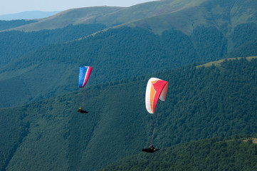 Paragliding in the sky. Two paraglider fly over the tops of the mountains in summer sunny day. Carpathians, Ukraine.