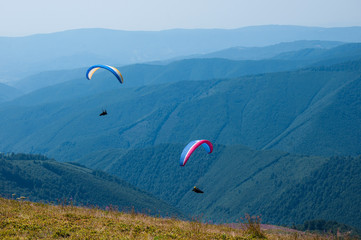 Paragliding in the sky. Two paraglider fly over the tops of the mountains in summer sunny day. Carpathians, Ukraine.