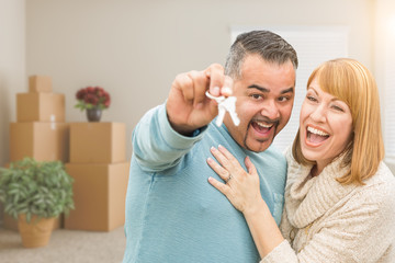 Mixed Race Couple Holding House Keys Inside Empty Room with Moving Boxes.