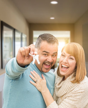 Mixed Race Couple Holding House Keys Inside Hallway of Their New Home.