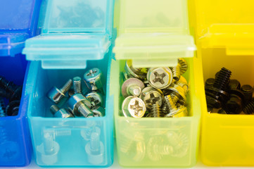 Different types of screws in small colored plastic containers. V