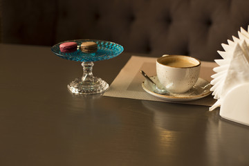 Colorful macaroons a cup and a ceramic cup of coffee with foam stands on a white napkin in a cafe in the sweet dark background color tone.