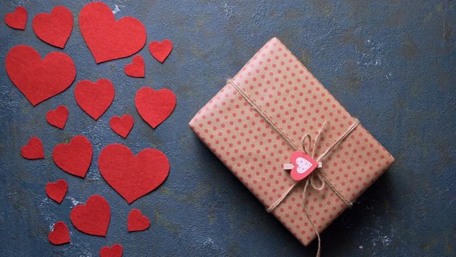 Woman presents Valentine's Day holiday gift box concept of romantic love. Vintage blue table with red hearts decorations flat lay. Blank space for design