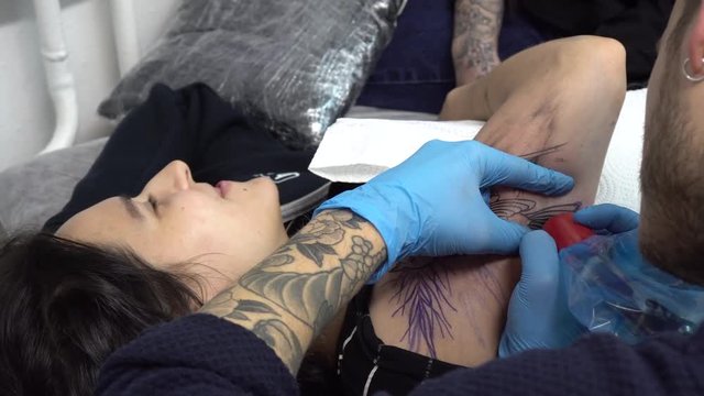 Tattoo artist tattooing young woman on the arm. Tattooer in medical sterile gloves