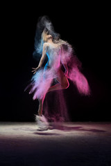 Young girl jumping in color dust cloud in studio