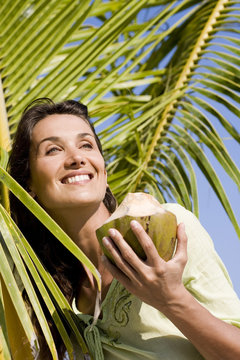 femme souriante avec une noix de coco sous un paimier