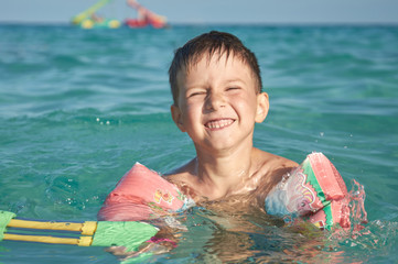 Boy with floater  sleeves swimming in a sea and having fun with water pistol